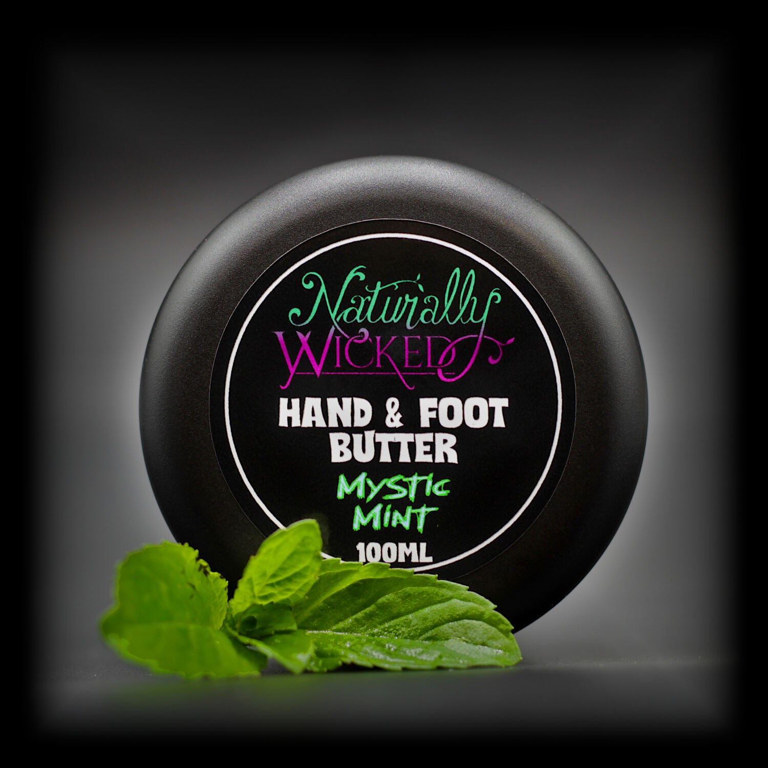 Naturally Wicked Mystic Mint Hand & Foot Butter Classy Black Lid Amongst Bright Green Fresh Mint Leaves