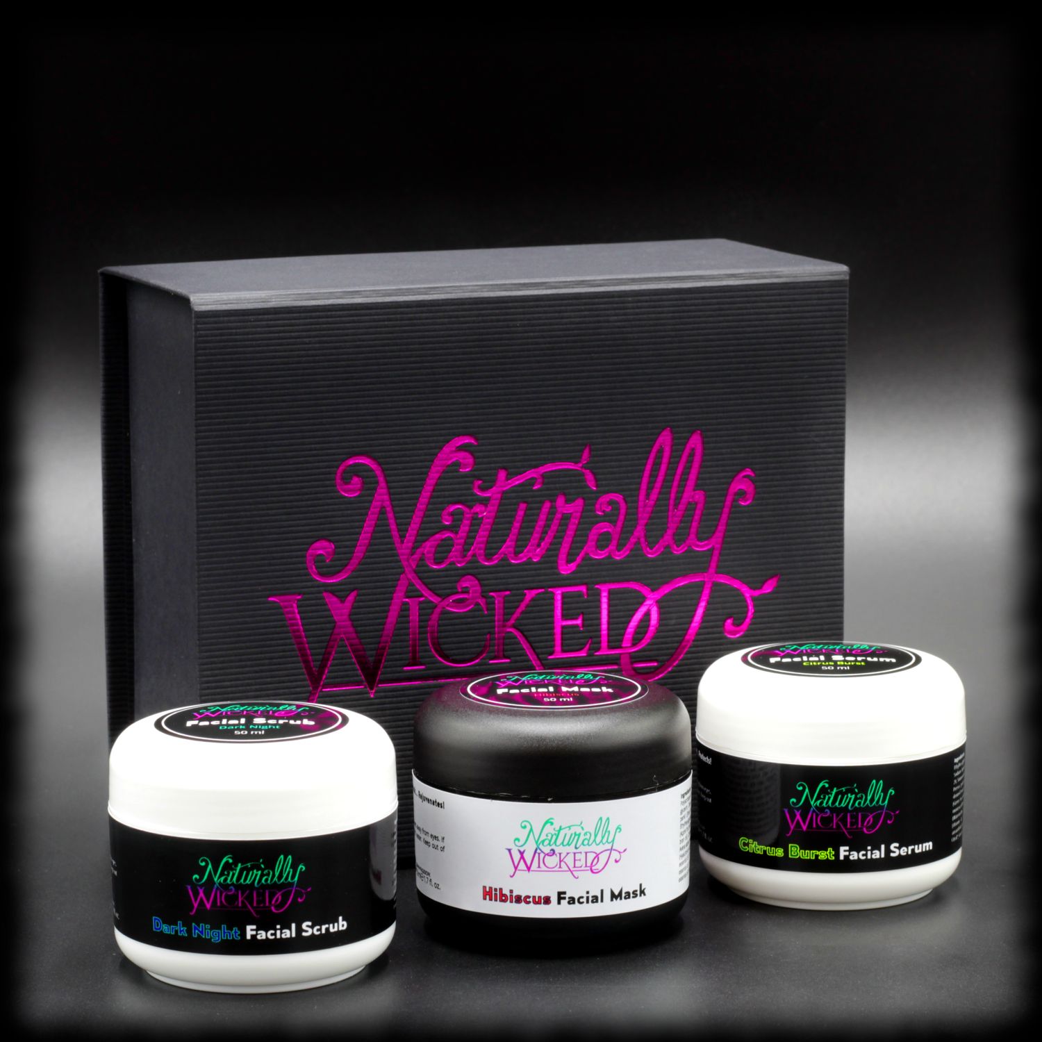 Naturally Wicked Original 3 Step Facial Kit With Dark Night Facial Scrub, Hibiscus Facial Mask & Citrus Burst Facial Serum In Front Of Original Pink & Black Box