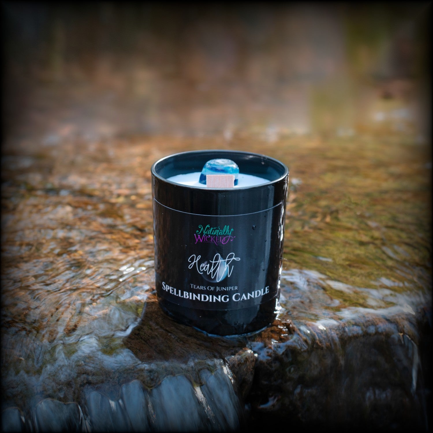 A Scenic View Of The Perfect Spell Candle situated in a crystal clear waterfall.  Naturally Wicked Spellbinding Health Candle Proudly Presents It's Dark Black Gloss Label With A Blue Water Tear On The Front. The Candle Features Plant-based Smooth Blue Wax, A Wood Wick And A Beautiful Teal Banded Agate Crystal. A Unique Gift For All