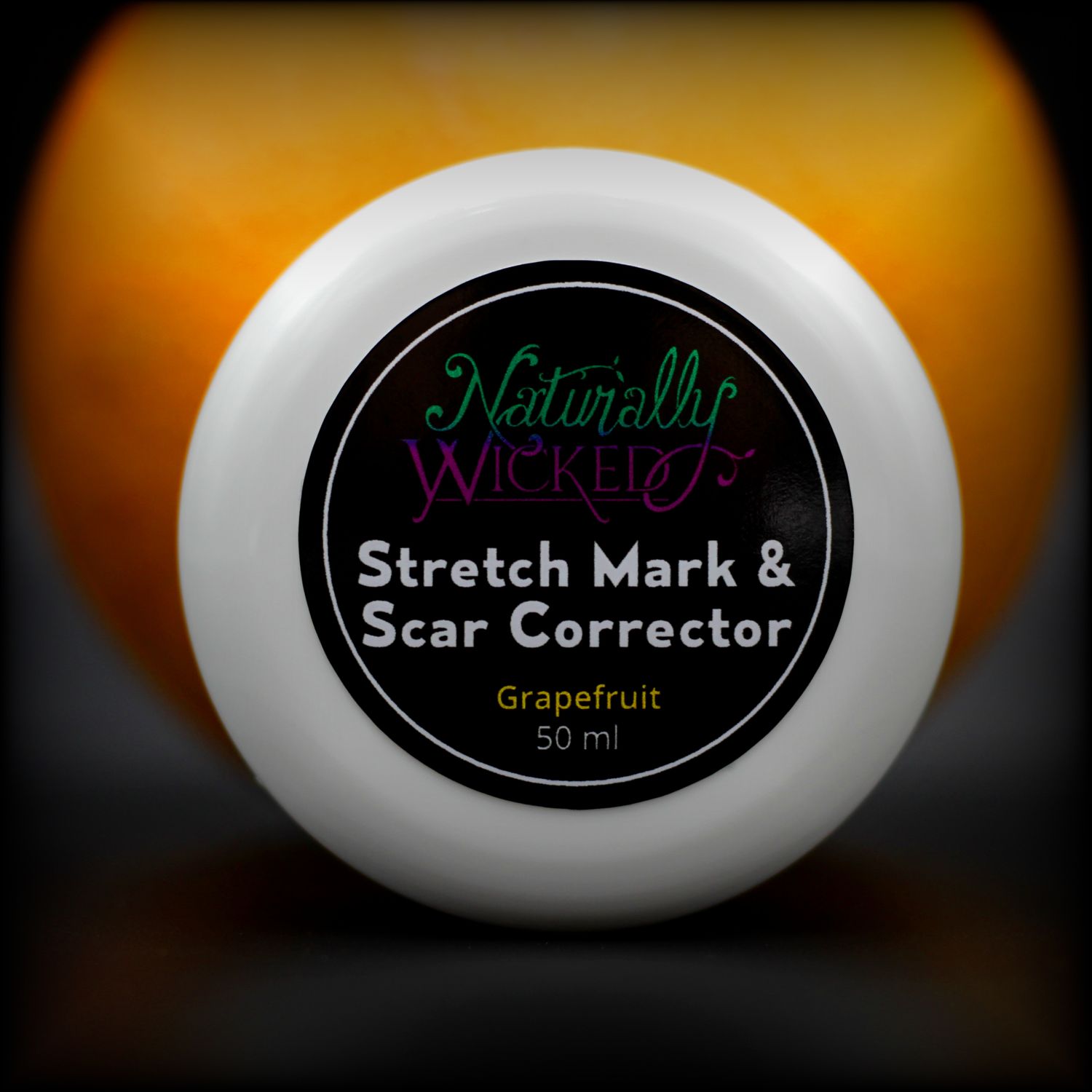 Naturally Wicked Stretch Mark & Scar Corrector Lid In Front Of A Whole Orange Grapefruit