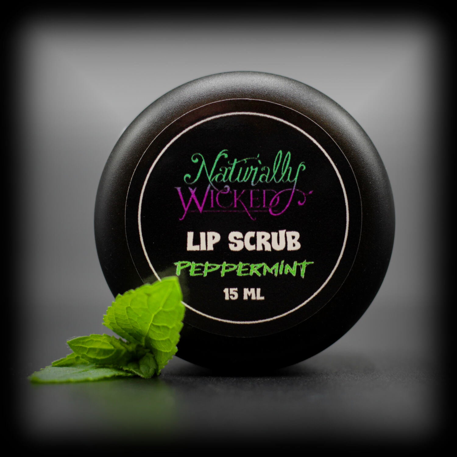 Naturally Wicked Peppermint Lip Scrub Luxury Labelled Lid Beside Bright Green Peppermint Leaf
