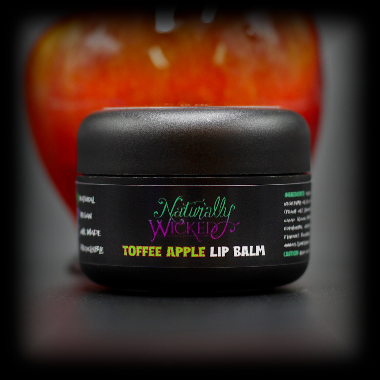 Naturally Wicked Toffee Apple Lip Balm In Front Of Rich Red Toffee Covered Apple