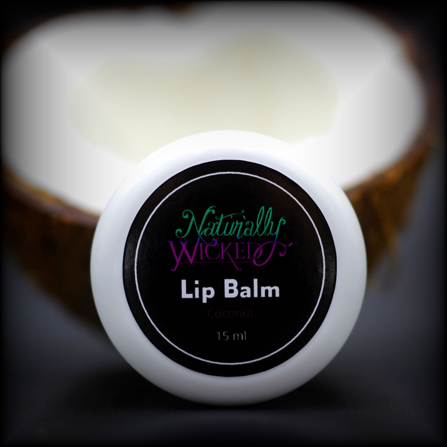 Naturally Wicked Coconut Lip Balm In Front Of Coconut With Visible Husk & Coconut Meat