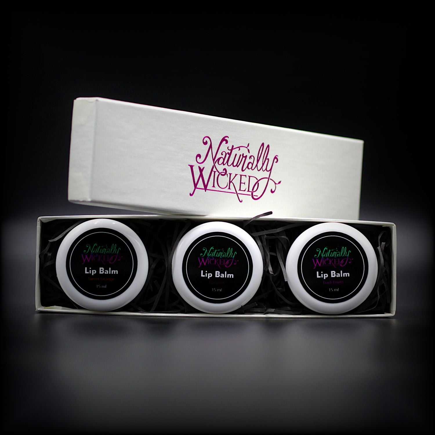 Naturally Wicked Lip Balm Trio Inner Box Revealed With Lids Of Orange, Dark Fruit & Coconut Lip Balm Peaking Out Amongst Luxury Gift Packaging