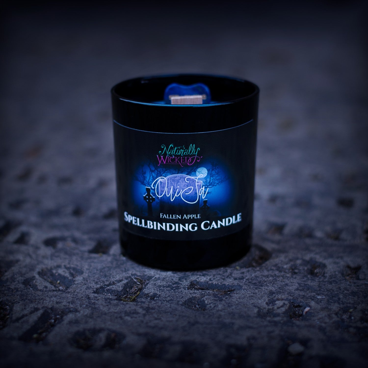 A Haunting View Of The Perfect Spell Candle Situated Within A Spooky Graveyard At Night. Naturally Wicked Spellbinding Ouija Candle Proudly Presents It's Dark Black Gloss Label With A Dark And Spooky Graveyard Design On The Front. The Candle Features Plant-based Smooth Blue Wax, A Wood Wick And A Beautiful Carved Sodalite Crystal Planchette.